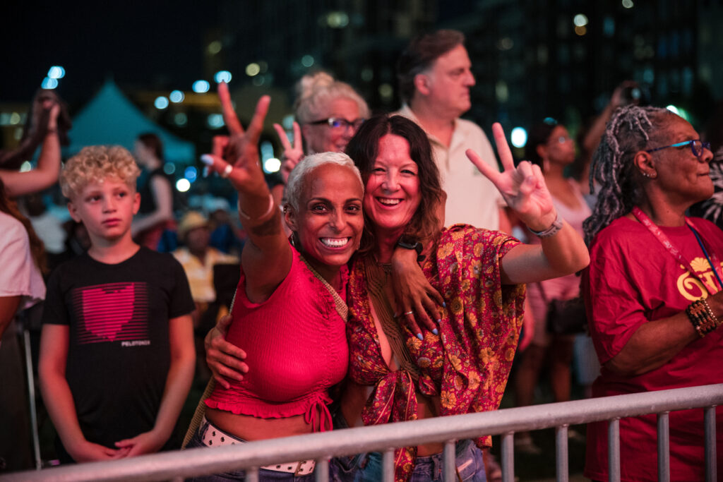 women smiling and giving peace signs at an outdoor concert